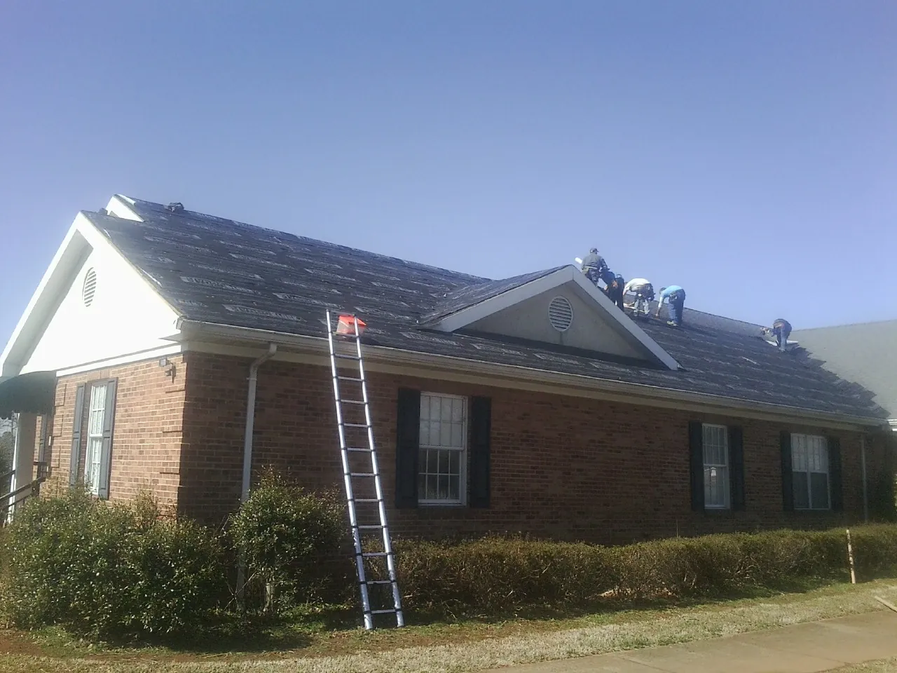 Crew tearing shingles off a brick ranch roof with a ladder set — Emergency Roof Repair work by our crew in Tioga