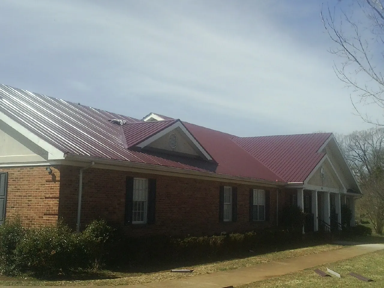 Red metal roof with gabled entries on a long brick building, from a Hail Damage Roof Repair job in Tioga