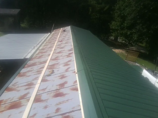 Old rusted panels beside newly installed green metal roofing — Wind Damage Roof Repair by Roofing Brothers in Tioga