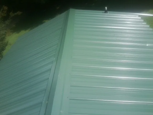 New green metal panels meeting at the ridge of a roof — Flat Roof Repair work by our crew in Tioga