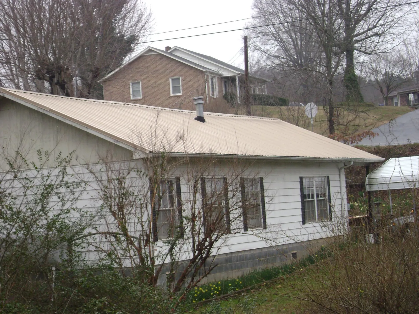 Tan metal roof on a white sided house set into a hillside — Commercial Roofing by Roofing Brothers in Tioga