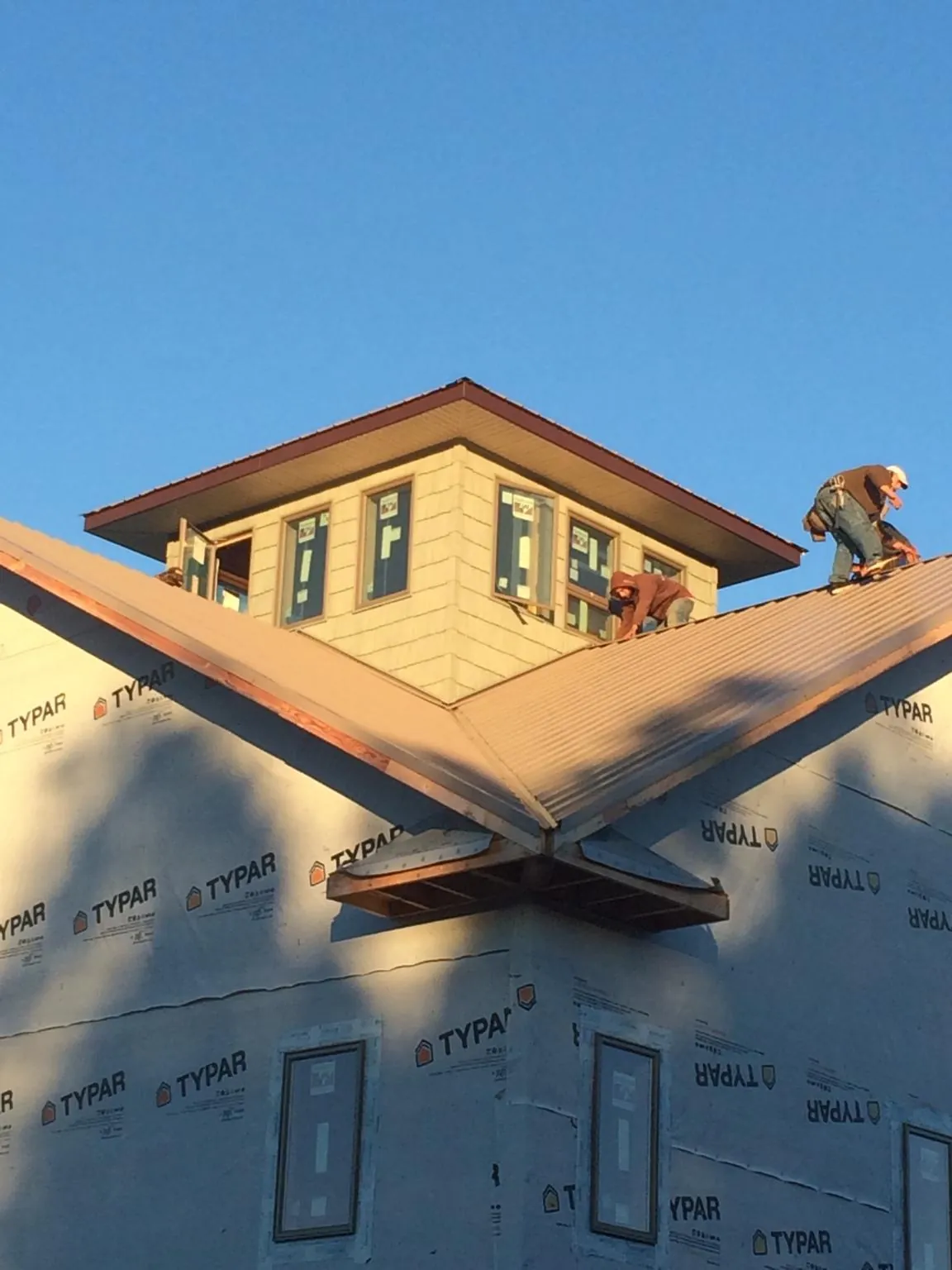Roofers working around a rooftop cupola on a new metal roof at sunset — Roof Waterproofing in Tioga by Roofing Brothers